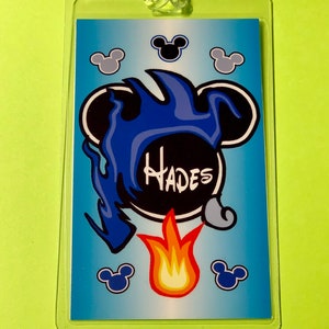 May include: A blue and black plastic luggage tag with a cartoon image of Hades from Disney's Hercules. The image features Hades's head with flames and the word "Hades" written in white.