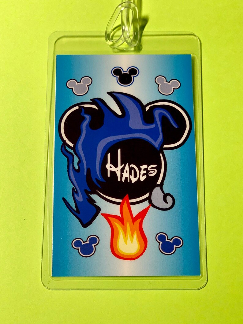 May include: A blue and black plastic luggage tag with a cartoon image of Hades from Disney's Hercules. The image features Hades's head with flames and the word "Hades" written in white.
