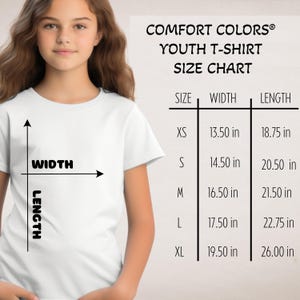 May include: A white youth t-shirt size chart from Comfort Colors. The chart shows sizes XS to XL with width and length measurements in inches. A young person is wearing a white t-shirt.