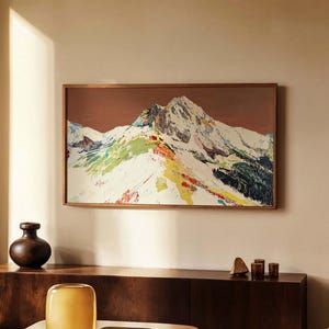 Puede incluir: Un interior de sala de estar con una mesa de café de madera, un jarrón y una pintura abstracta enmarcada de una cordillera con acentos coloridos. La pintura está colgada en una pared beige.