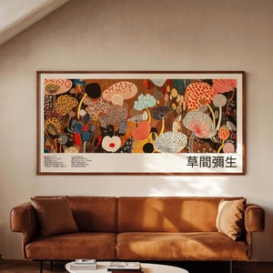 Puede incluir: Un sofá de cuero marrón con dos almohadas se encuentra frente a una impresión enmarcada de coloridas setas. La impresión tiene texto japonés que dice "草間彌生".