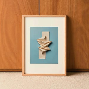 Può includere: Opera d'arte astratta incorniciata. Sfondo azzurro chiaro con un rettangolo beige verticale. Forme di carta piegate sovrapposte, in tonalità beige, sono al centro. L'opera è in una cornice in legno naturale, per l'arredamento.