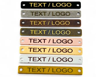 May include: Eight metal tags with a hole at each end. The tags are in different colours: black, grey, brown, antique gold, rose gold, gold, silver, and yellow gold. Each tag has the text "TEXT/LOGO" engraved on it.