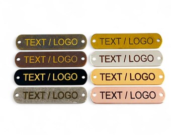 May include: Eight metal tags with rounded edges and two holes. The tags are in different colours: antique brass, copper, black, silver, and rose gold. Each tag has the text "TEXT/LOGO" engraved in gold.