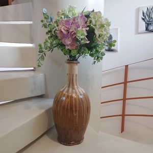 Peut inclure: Un vase en céramique brun avec des rayures blanches et un bouquet de fleurs roses et blanches.