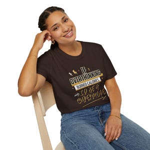 Puede incluir: Una camiseta de manga corta de color marrón oscuro con el texto en blanco y amarillo "IF OVERTHINKING BURNED CALORIES, I'D BE A SUPERMODEL" junto con pequeños detalles gráficos de rayos y estrellas impresos en la parte frontal de la prenda.