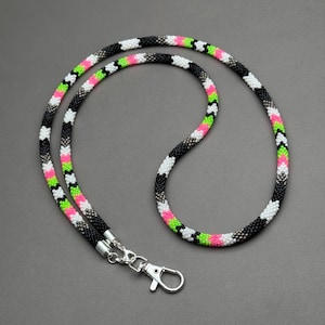 May include: A black, white, pink, and green beaded lanyard with a silver swivel clasp.