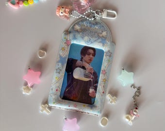 May include: A clear acrylic card holder with a photo of a person pouring liquid into a glass. The holder is decorated with pastel stars and a beaded keychain with the name "JUNG" spelled out. Additional charms include a pink bow and star-shaped pendants.