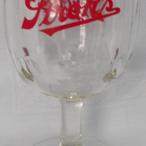 May include: Clear glass goblet with a rounded bowl and a stem. The word "Archie's" is printed in red script across the bowl. The goblet has a wide base and is likely used for serving beverages.