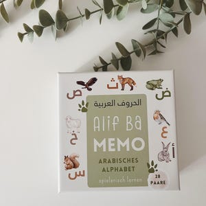 Könnte beinhalten: Alif Ba Memo Spielbox mit grünem Hintergrund und Tierillustrationen. Die Box zeigt das arabische Alphabet und den Text "Alif Ba Memo" in Weiß. Der Text "Arabisches Alphabet" und "spielerisch lernen" ist ebenfalls auf der Box zu sehen.
