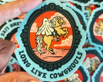 Può includere: Un mucchio di adesivi con un fantasma dei cartoni animati che cavalca un cavallo, su uno sfondo rosso e arancione. Gli adesivi hanno un bordo azzurro e il testo "LONG LIVE COWGHOULS".