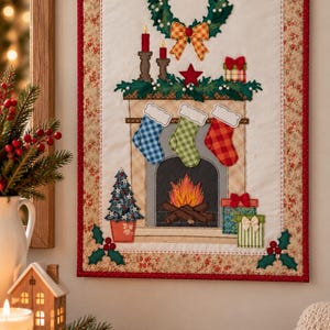 May include: A rectangular fabric wall hanging featuring a quilted Christmas scene. The design includes a fireplace with three hanging stockings, a wreath, a burning fire, a small tree, and wrapped gifts, all framed by a floral border.