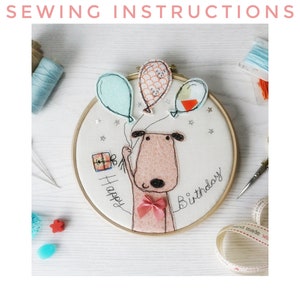 May include: Embroidered hoop art featuring a brown dog holding a gift box and balloons. The hoop is decorated with stars and the text "Happy Birthday".