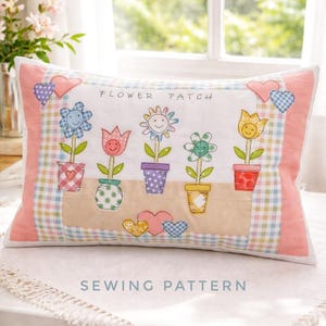 May include: Rectangular pillow with a floral design. The pillow features embroidered flowers in pots with smiling faces, set against a white background. The words "FLOWER PATCH" and "SEWING PATTERN" are printed on the pillow.