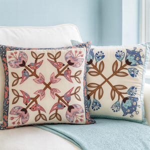 May include: Two decorative cushions with floral and bird designs. The cushions have a cream background with embroidered brown branches and pink, blue, and brown floral and bird motifs. The edges are trimmed with a patterned fabric.