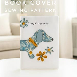 Puede incluir: Cubierta de libro blanca con un diseño de perro salchicha en tela floral azul, un collar amarillo y detalles de margaritas. El texto "Paws for thought" está escrito en la cubierta. Las palabras "BOOK COVER SEWING PATTERN" están en la parte superior.
