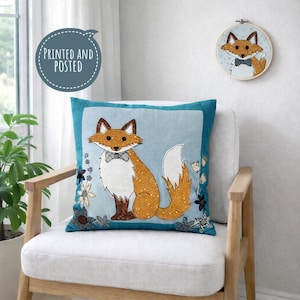 May include: A teal square cushion featuring an embroidered fox design with a bow tie, set against a light blue backdrop. A matching fox embroidery hoop is on the wall. The text "PRINTED AND POSTED" is in a circle. The cushion is on a white chair.