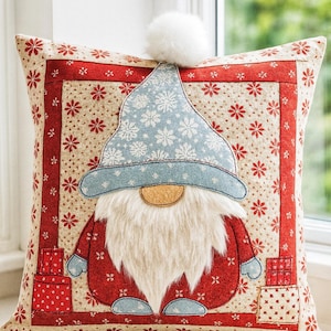 May include: A decorative square pillow featuring a gnome design. The gnome has a light blue hat with white snowflakes, a white beard, and a red coat. The pillow has a red border and a beige background with red floral patterns. A white pom-pom is on top.
