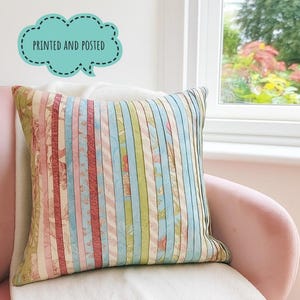 May include: A square cushion with vertical stripes in pastel shades of pink, blue, and green. Some stripes feature a floral design. The cushion has the text "PRINTED AND POSTED" in a speech bubble.