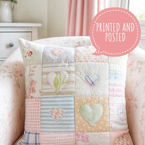 May include: A patchwork cushion with pastel fabrics, including floral, striped, and gingham patterns. Each square features a heart applique. The cushion is on a floral patterned chair. The text "PRINTED AND POSTED" is in a pink speech bubble.