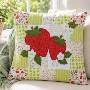 May include: A square scatter cushion featuring a patchwork design with various patterns of strawberries and green apples. The centre displays two large red strawberry appliqués with green leaves and white flowers on a white background with text.