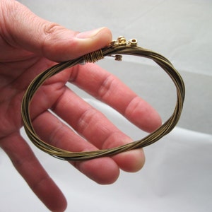 May include: A close-up of a gold guitar string bracelet. The bracelet is made of multiple guitar strings that have been woven together.