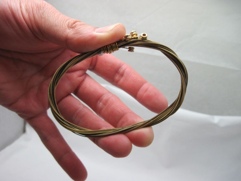 May include: A close-up of a gold guitar string bracelet. The bracelet is made of multiple guitar strings that have been woven together.