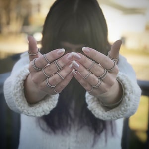 May include: A person's hands wearing multiple silver rings on each finger. The rings are stacked on top of each other and are all different sizes.