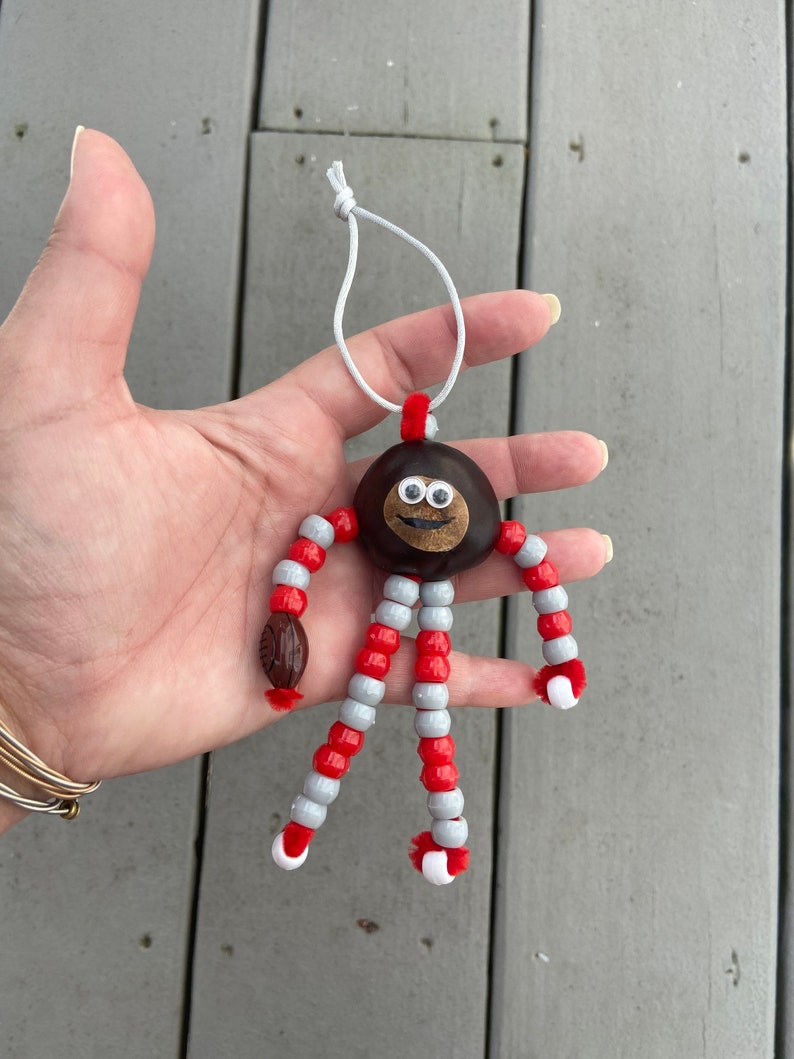 May include: A chestnut with googly eyes and a smiling mouth is strung with red and white beads to create a whimsical ornament.