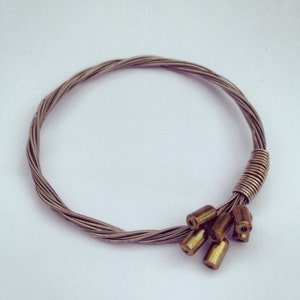 May include: A silver guitar string bracelet with a cluster of gold-toned beads at the end.
