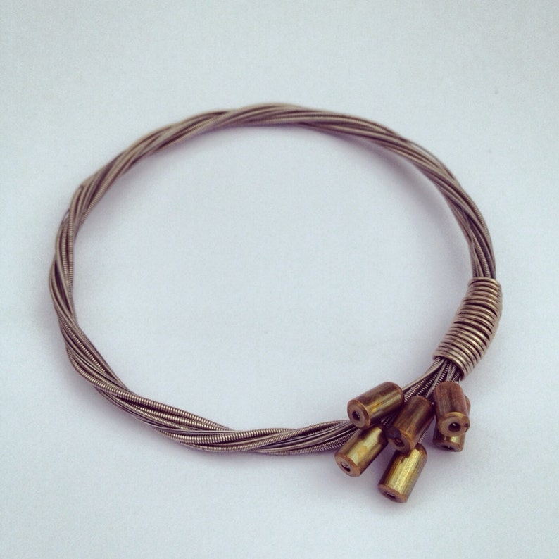 May include: A silver guitar string bracelet with a cluster of gold-toned beads at the end.