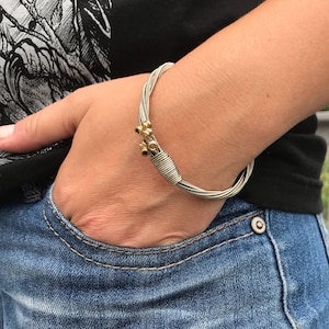 May include: A silver guitar string bracelet with gold beads. The bracelet is worn on a person's wrist.