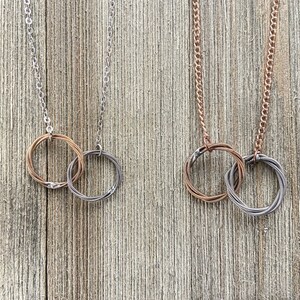 May include: Two necklaces made from intertwined guitar strings. One necklace is silver and the other is copper.