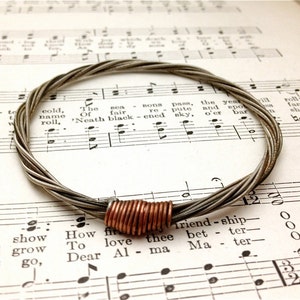 May include: A silver guitar string bracelet with a copper accent. The bracelet is lying on a sheet of music.