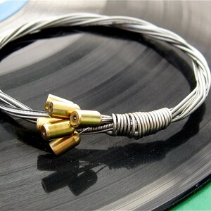 May include: A silver guitar string bracelet with a cluster of gold-toned metal beads.