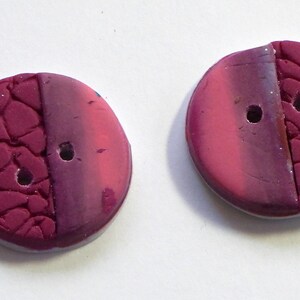 May include: Two round, pink and purple buttons with a textured design. One side of each button has a smooth, ombre finish, while the other side has a textured, cracked finish.