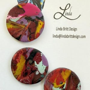 May include: Three colorful, round buttons with a marbled design. The buttons are red, yellow, purple, black, and white. The buttons are made of polymer clay and have a glossy finish. "Buttons as Individual as You!" and "Linda Britt Design" are written on the card.