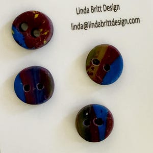May include: Four round buttons with two holes each, featuring a marbled pattern of deep red, blue, and yellow. The buttons are attached to a white display card printed with the text Linda Britt Design and linda@lindabrittdesign.com.