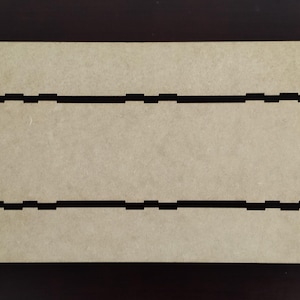 Op de afbeelding: Ongemonteerde houten dooscomponenten, met een rechthoekige basis en zijpanelen met in elkaar grijpende lipjes. De stukken zijn lichtbruin van kleur, met donkerbruine snijlijnen. Het ontwerp suggereert een doe-het-zelf project.