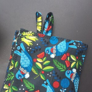 May include: A black fabric pot holder with a colorful pattern of birds, leaves, and berries. The pot holder has a loop for hanging.