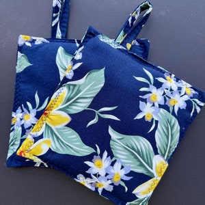 May include: Two blue pot holders with a floral pattern of white and yellow flowers and green leaves. The pot holders have a loop handle.