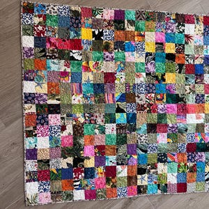 May include: A colourful patchwork quilt featuring a range of floral and geometric patterns. The quilt is composed of numerous small squares, each with a unique design. The quilt is a vibrant blend of colours, including red, green, blue, yellow, and purple.