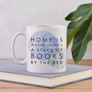 May include: White ceramic mug with a blue and gray marbled design. The mug has the text "Home is where there's a stack of books by the bed."