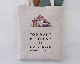 Puede incluir: Una bolsa de tela beige con un gráfico de una pila de libros y un jarrón de flores. El texto en la bolsa dice "¿Demasiados libros? ¿O no suficientes estanterías?"
