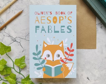 May include: A blue card with the text "Oliver's Book of Aesop's Fables" in yellow and brown letters. A cartoon fox is holding a blue book with a red cover. The fox is surrounded by green and red leaves.