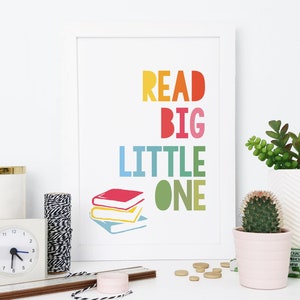 May include: A white framed print with the text "READ BIG LITTLE ONE" in rainbow colors. The print features a stack of three colorful books.