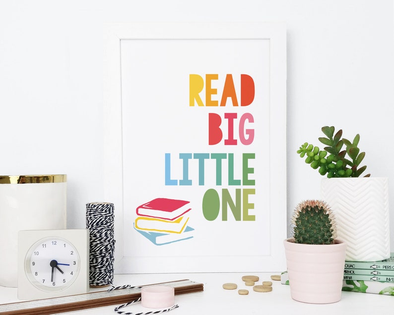 May include: A white framed print with the text "READ BIG LITTLE ONE" in rainbow colors. The print features a stack of three colorful books.
