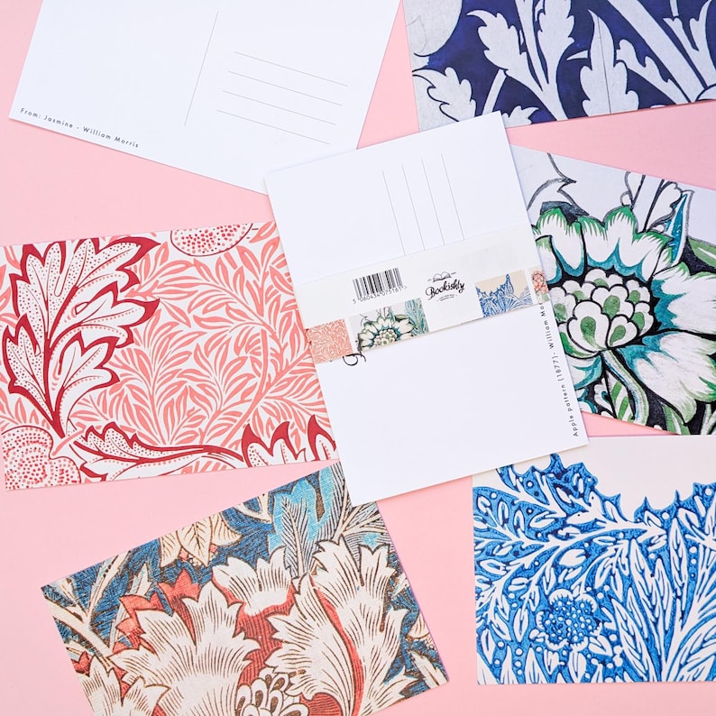 May include: A collection of postcards with floral patterns in shades of red, blue, and green, arranged on a pink surface. The postcards feature intricate designs and the text "From: Jasmine - William Morris" and "Apple pattern (1877) William Morris".