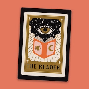 May include: A tarot card with a black background and gold accents. The card features an open book with a sun and moon on the cover. Above the book is a large eye with a brown iris and a black pupil. The card is titled "THE READER".