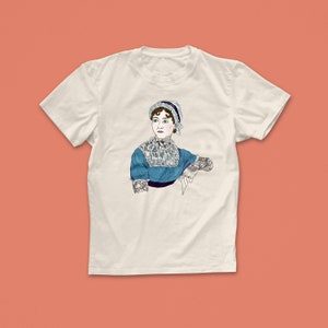 Pu&ograve; includere: Una maglietta bianca con una grafica di Jane Austen con tatuaggi. La grafica &egrave; a colori e mostra Austen con un vestito blu e un cappello bianco.